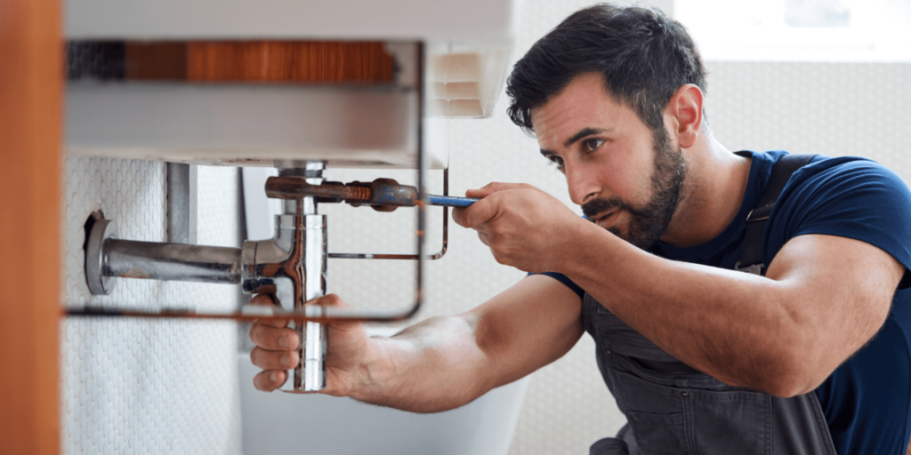 A professional plumber fixing a leaking kitchen sink with a toolbox nearby.