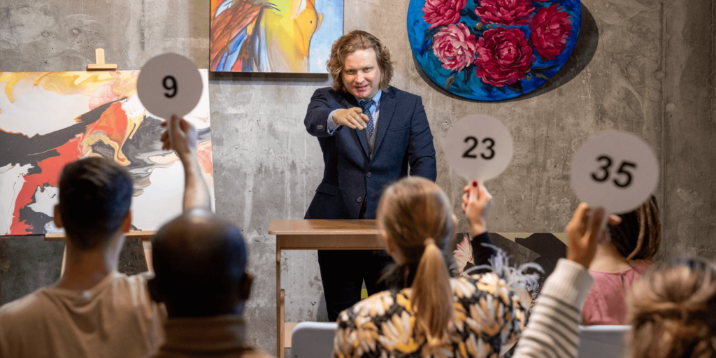 Auctioneer in a suit conducting a live auction while participants raise numbered paddles.